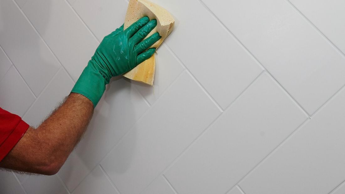 A sponge being used to spread grout into gaps between tiles on a wet wall