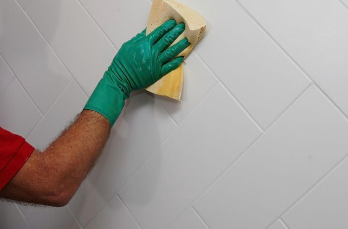 A sponge being used to spread grout into gaps between tiles on a wet wall