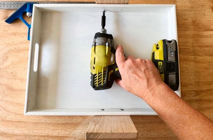 A person using a drill to secure button head screws in a MDF tray.