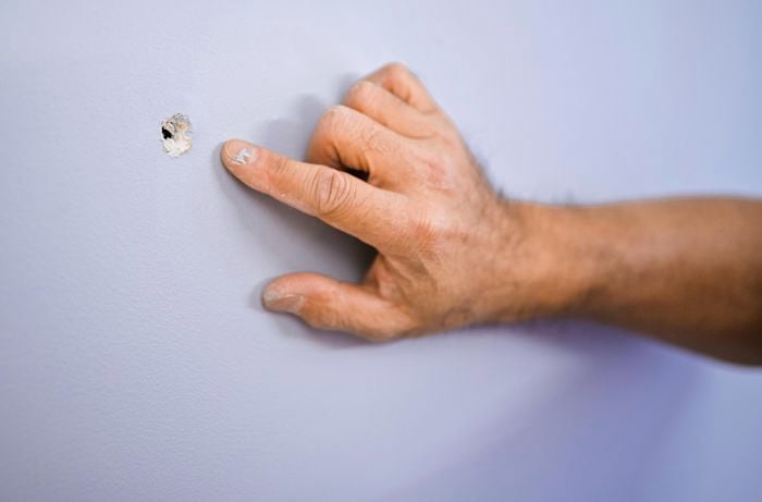 A person pointing to a hole in a wall