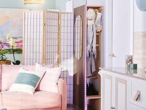Close up of the corner of an entryway with a compact cloakroom/mudroom at the entrance, a free-standing divider, and a pale pink lounge