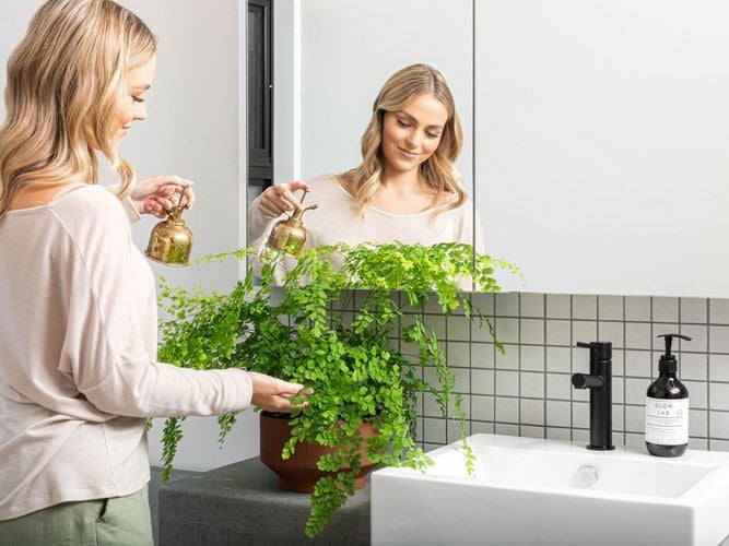 lady in bathroom watering her green potting fern