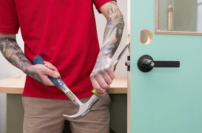 A person is using a hammer and chisel to create a recess on the door edge for a latch.