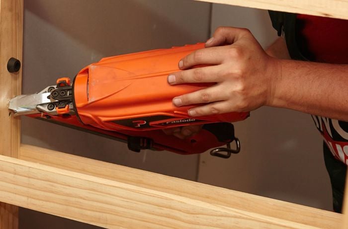 A person using a nail gun to fix a door frame to a wall stud
