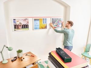 Person hanging a picture on the wall in line with two other pictures.
