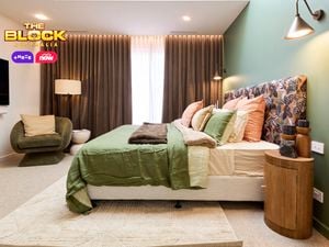 Bedroom with green feature wall, patterned headboard, and layered bedding.
