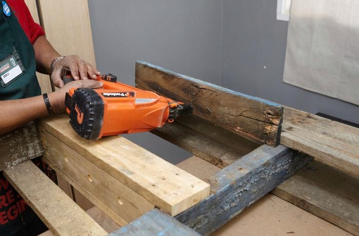 A person fixing a shelf into a timber frame using a nail gun
