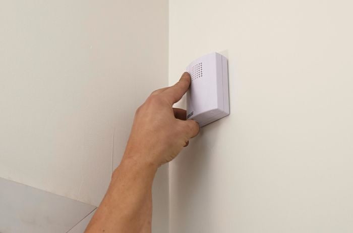 A person attaching a doorbell receiver unit to an interior wall