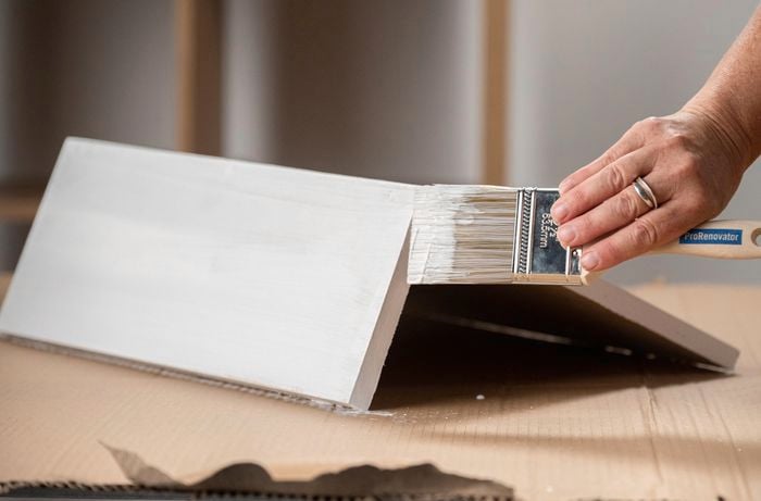 A person with a paint brush painting a piece of wood