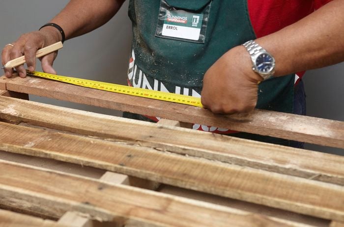 Person measuring and marking timber slats with tape measure and pencil