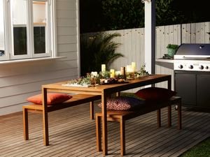 Outdoor dining table set with candles, greenery and cheese board with BBQ in the background.