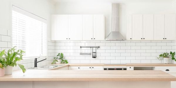 A kitchen with a timber benchtop, white cabinets and a white tiled splashback.