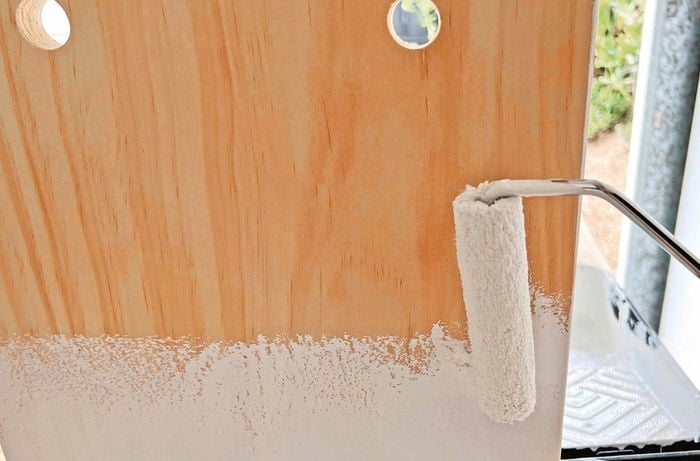 Paint roller applying white paint onto wood.