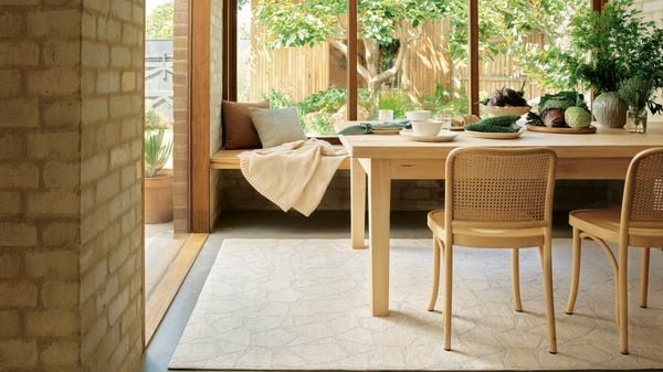 Sunlit dining area with timber table, woven chairs, and garden view