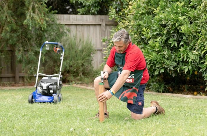 Bunnings team member kneeling down using a hammer on a garden stake