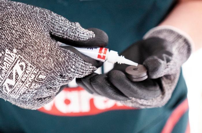 Superglue being applied to the back of a magnet by a Bunnings team member wearing protective gloves