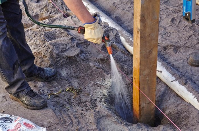 Water being added to a posthole filled with dry concrete for the purpose of setting in place a new post