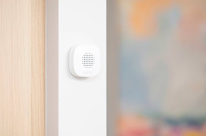 A Swann chime device is mounted on an indoor wall next to a wooden door frame