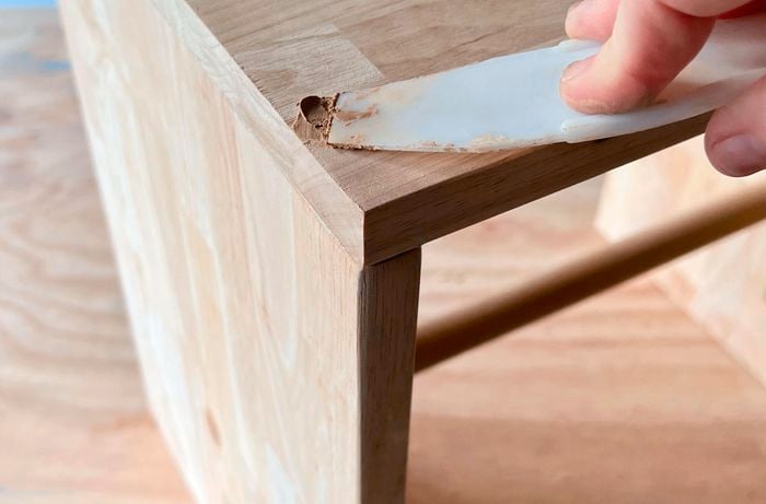 Close up of a hand using a scraper to fill drill holes in a timber table with filler