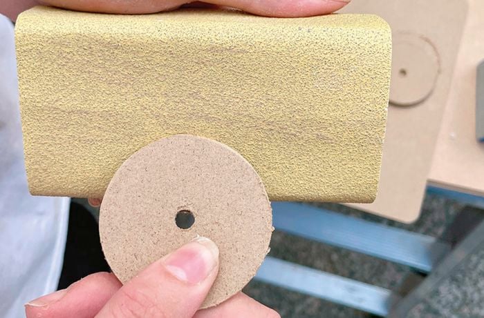 A person smoothing the edges of an MDF disc on 180-grit abrasive paper.