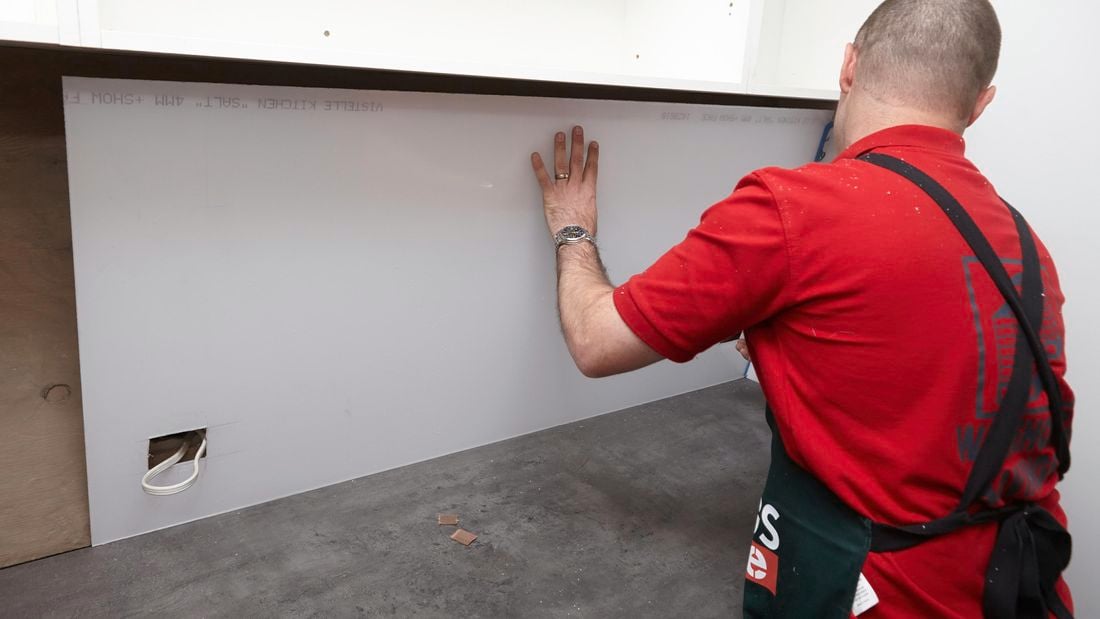 A splashback being fixed to a wall by a Bunnings team member