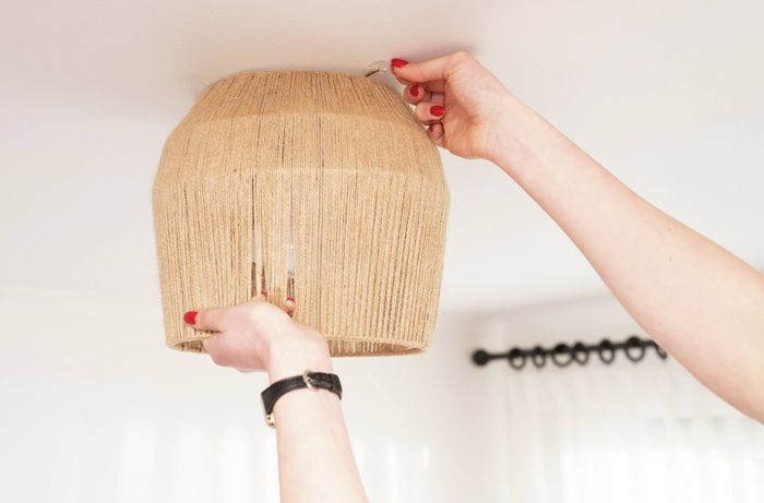 : A person is sliding a woven basket over a pendant fitting to check the height, alignment and bulb clearance before installation. 