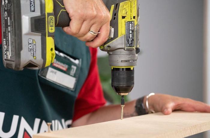 A Bunnings Team Member holding a cordless drill, drilling a screw into a piece of wood