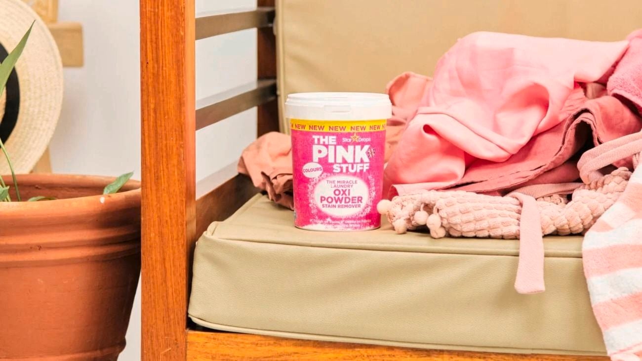 A tub of The Pink Stuff sitting on a timber chair next to a pot plant.