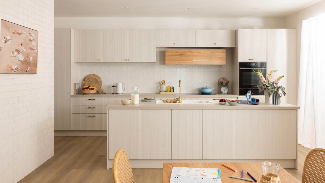 Soft Coastal kitchen with light groove cabinets, timber rangehood, gold tapware, and airy natural light