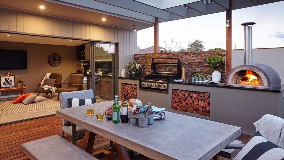 An outdoor room with wood-fired pizza oven, BBQ and furniture looking into a living room