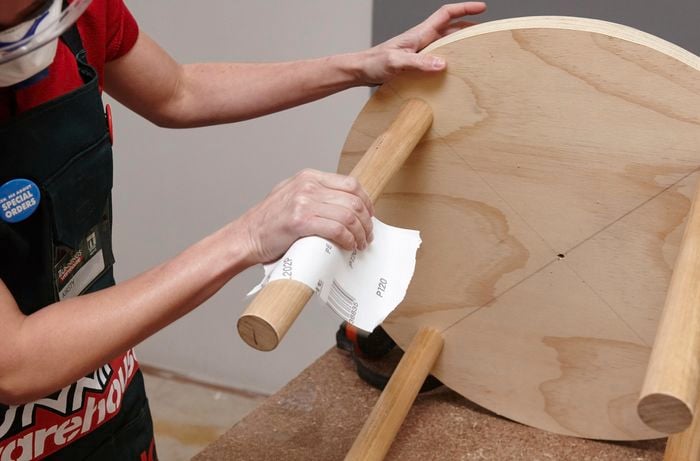 A person sanding a dowel leg on a round table