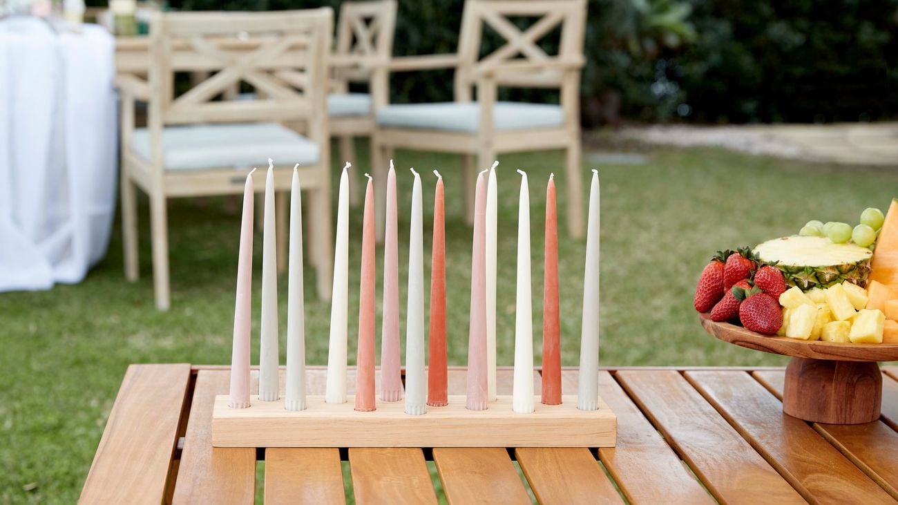 D.I.Y candlestick holder with an array of white, pink, red and green candlesticks sitting on an outdoor coffee table.