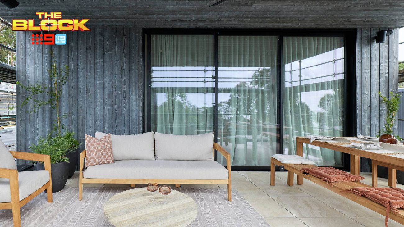 Covered outdoor entertaining area featuring a timber-framed sofa, stone coffee table and dining setting beside large glass doors.