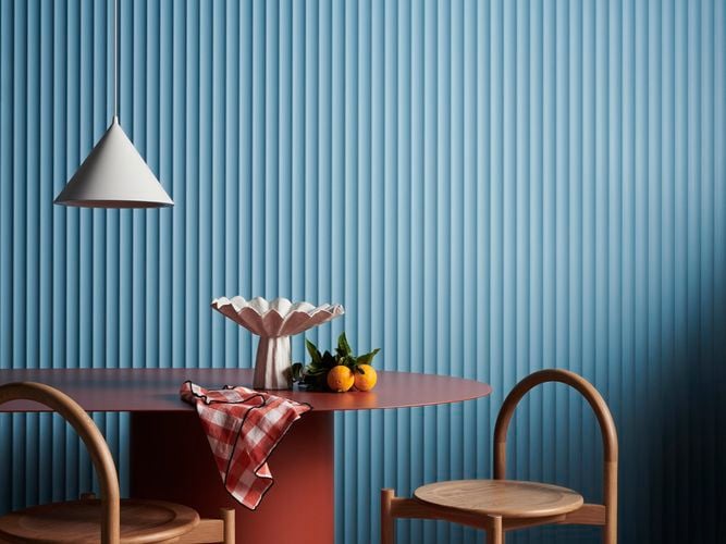 A hanging lamp, table and two chair in front of a blue Laminex wall.