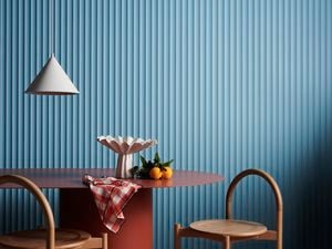 A hanging lamp, table and two chair in front of a blue Laminex wall.