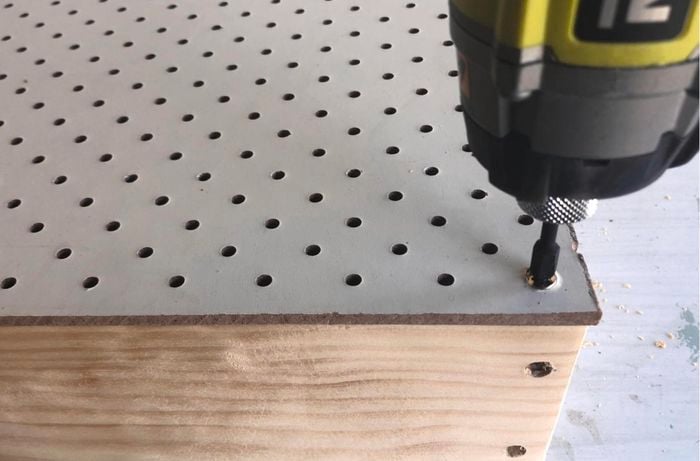 Person drilling through pegboard wall sheet.