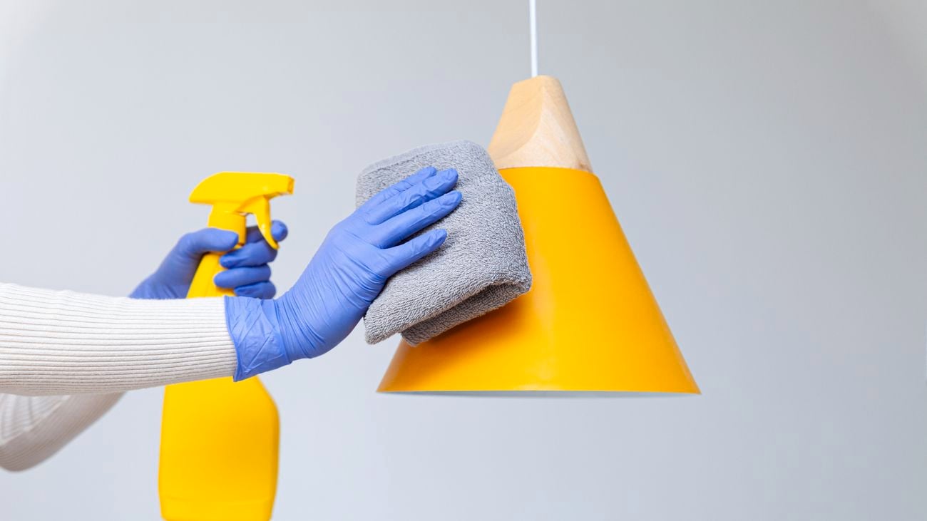 Hands in rubber gloves removing dust, cleaning yellow pendant lamp
