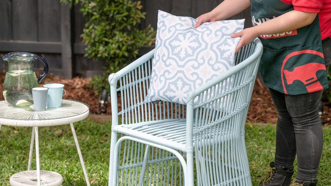 Bunnings team member styling the wicker chair with a matching cushion and outdoor coffee table with a jug of water and cups