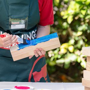 Bunnings team member painting a piece of timber with blue paint