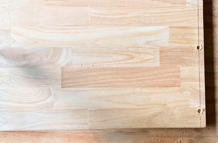 A rectangular panel of timber being drilled with holes into the edges
