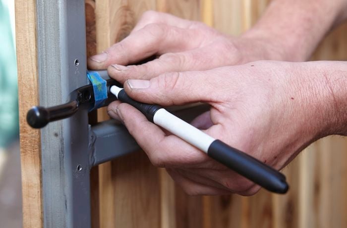 Person using permanent marker to mark screw points in gate latch.