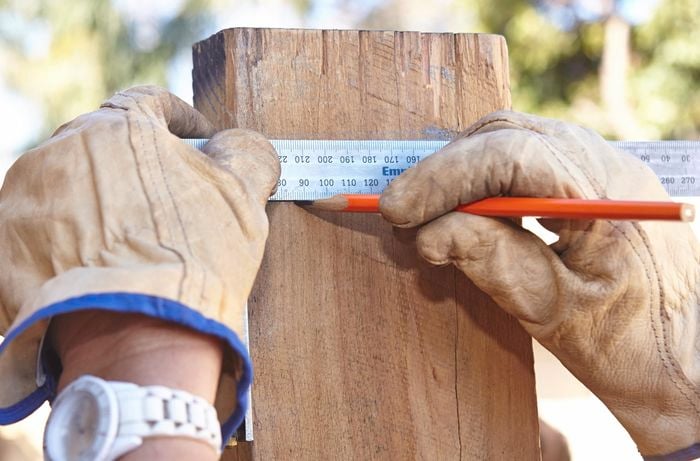 Person measuring weathered plinth with metal ruler and measuring tape.