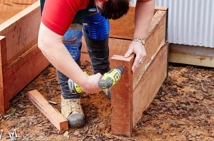 Front guides being secured to the front of a sleeper compost bin with a power drill