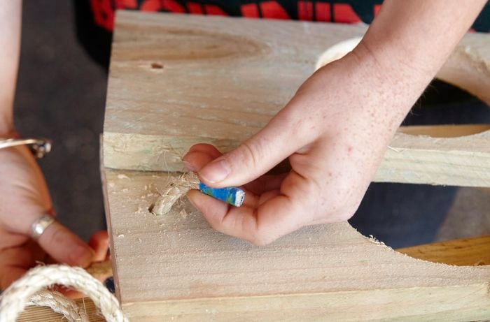 A person threading rope through a hole in a pine board