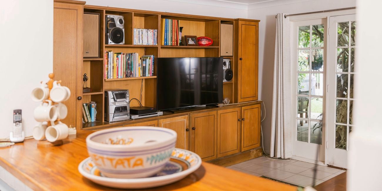 Living room with wooden entertainment cabinetry, bookshelves, a television, and glass doors leading outside.
