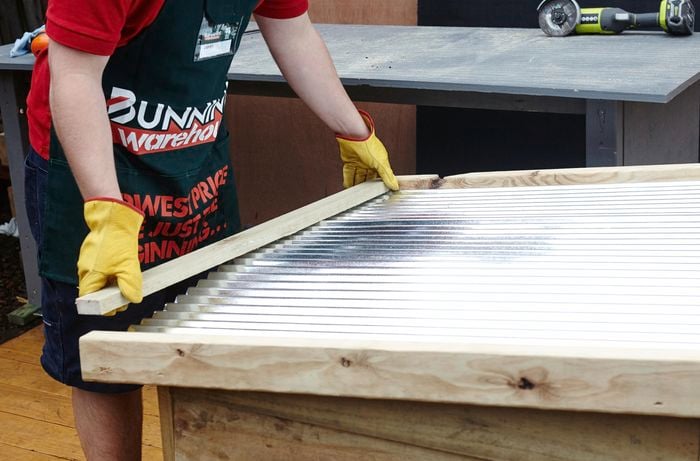 Person placing piece of timber on top of metal roof of DIY dog kennel.