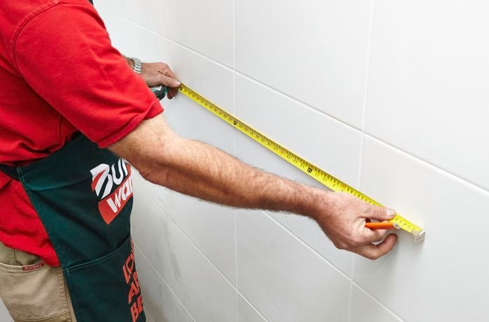 A person measuring a white tiled wall