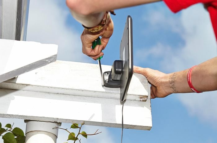 A person using a screwdriver to mount a solar panel on the beam of a pergola 