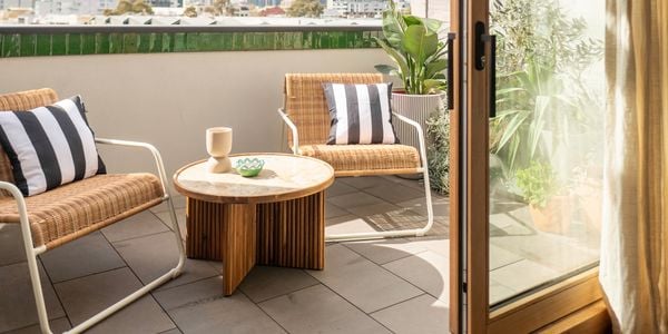 A cozy outdoor corner with wicker chairs, colorful cushions, and various potted plants creating a relaxing, nature-inspired ambiance.