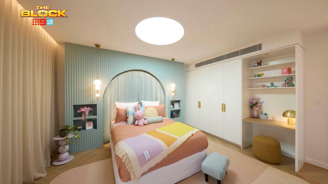 Pastel bedroom featuring a pale blue feature wall with recessed bedside tables and a double bed with pastel linen in orange, purple and yellow. 